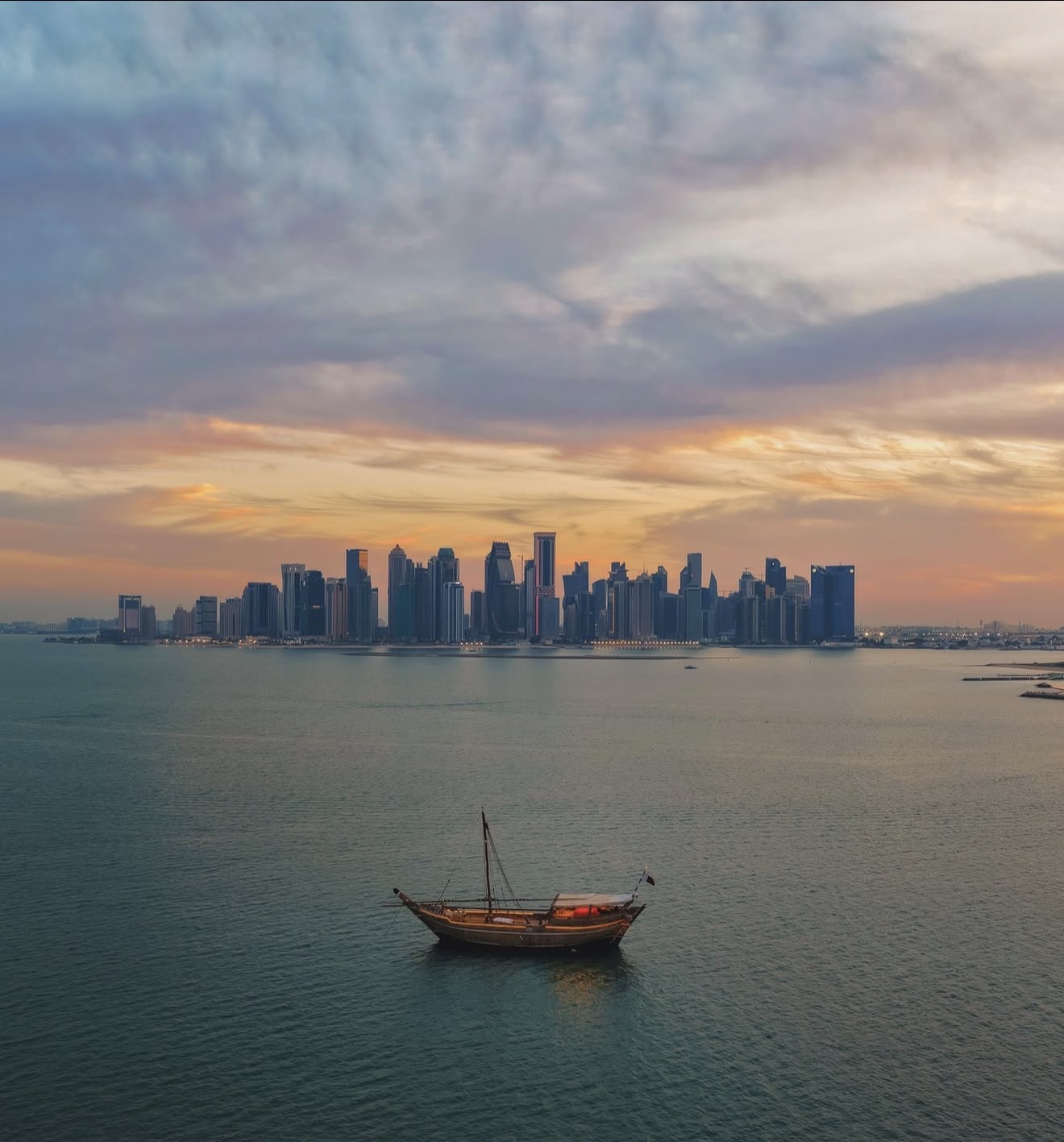 Traditional dhow floating before Doha's skyline at sunset