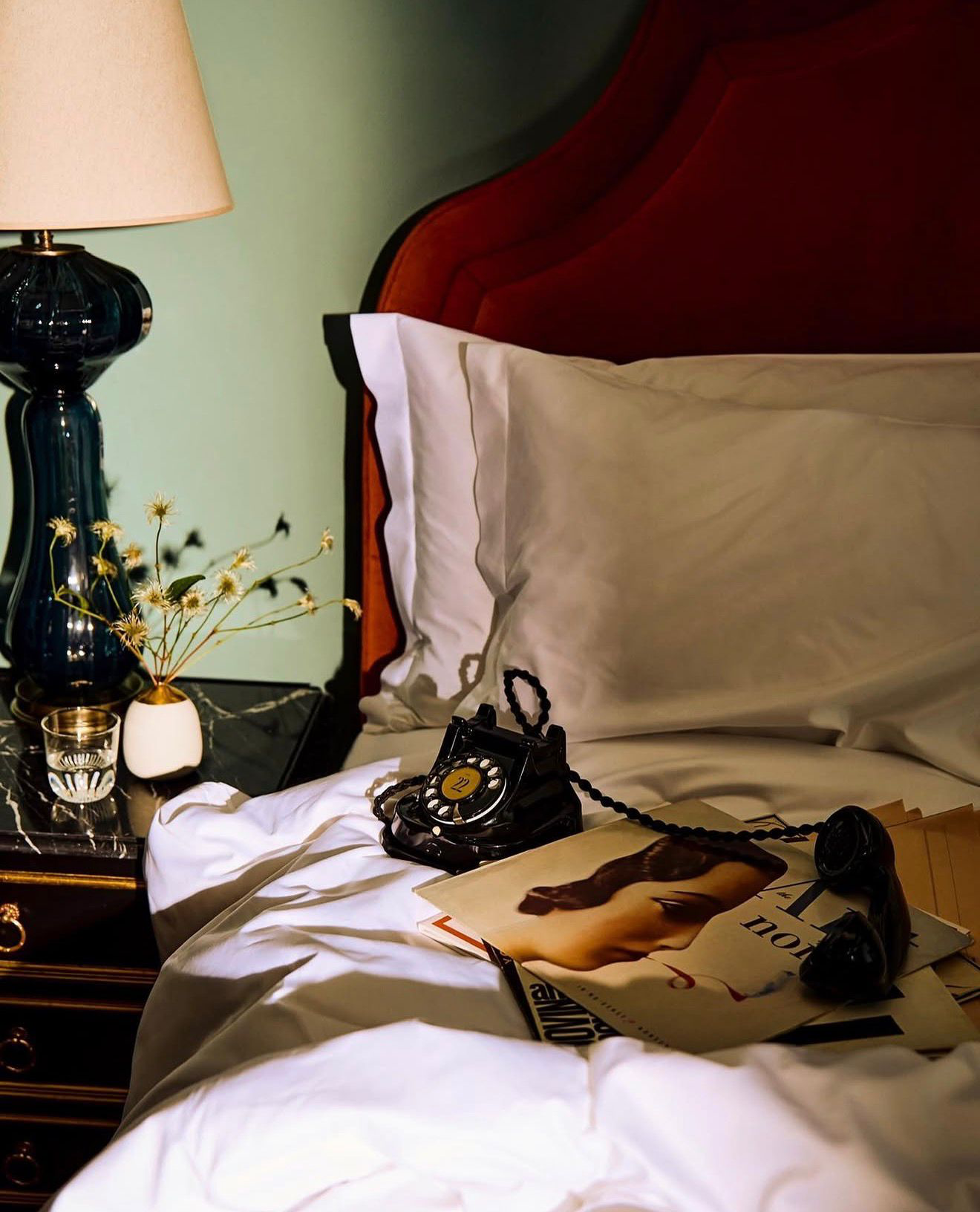 A vintage black rotary telephone resting on crisp white linens beside a lit bedside lamp