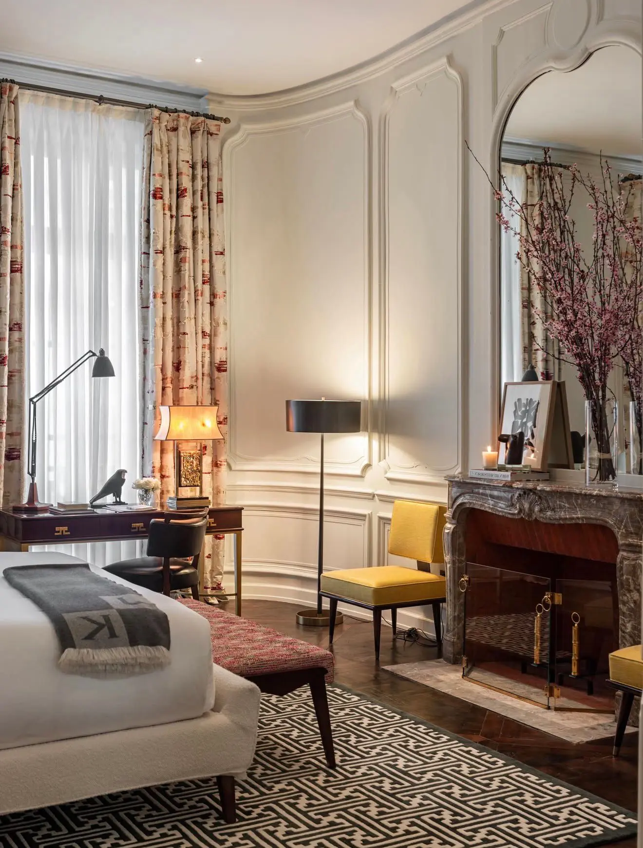 A refined cream bedroom sitting room with a marble fireplace, yellow chair and mirrored wall