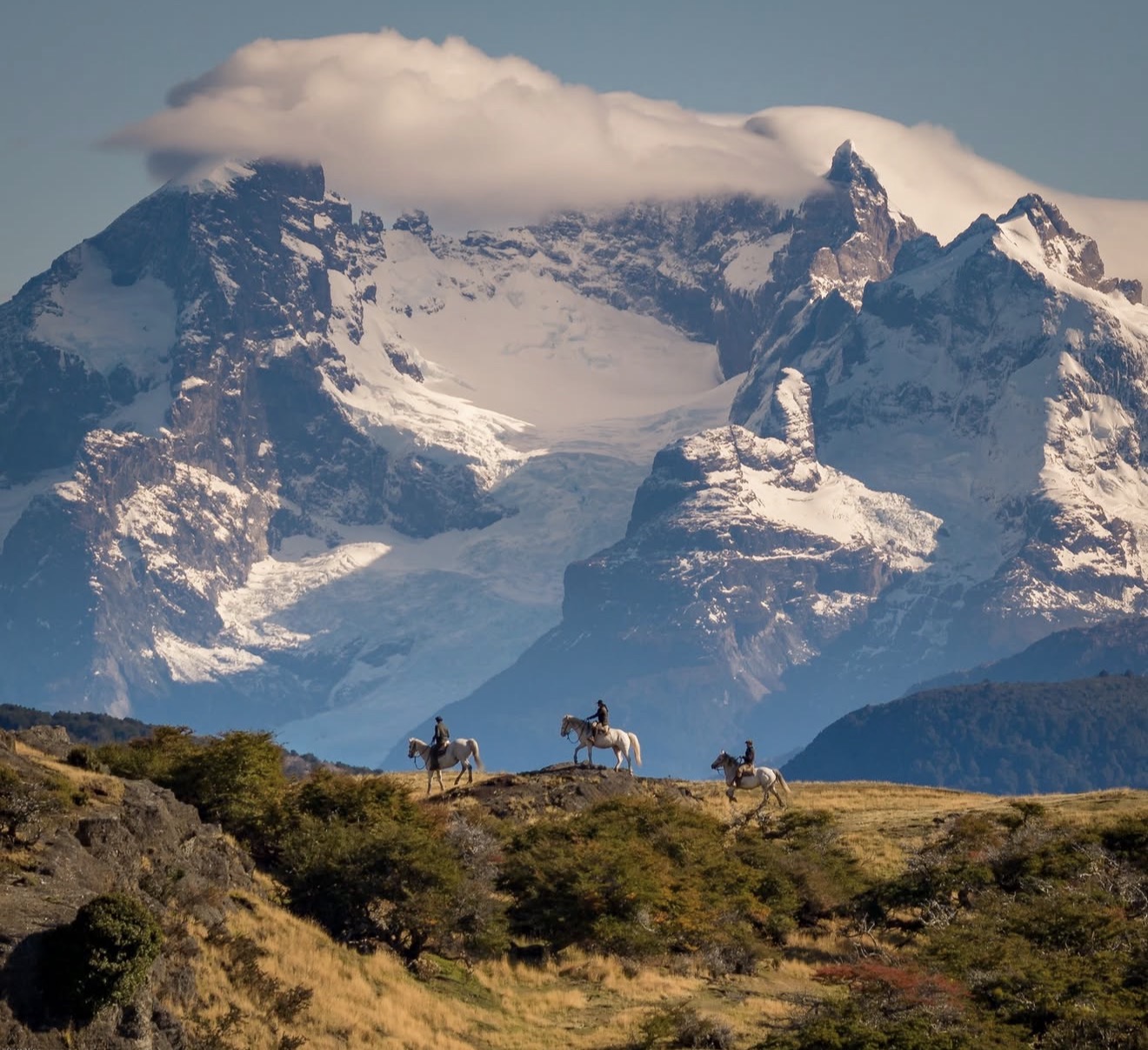 Riders crossing the Patagonian steppe beneath snow-covered peaks
