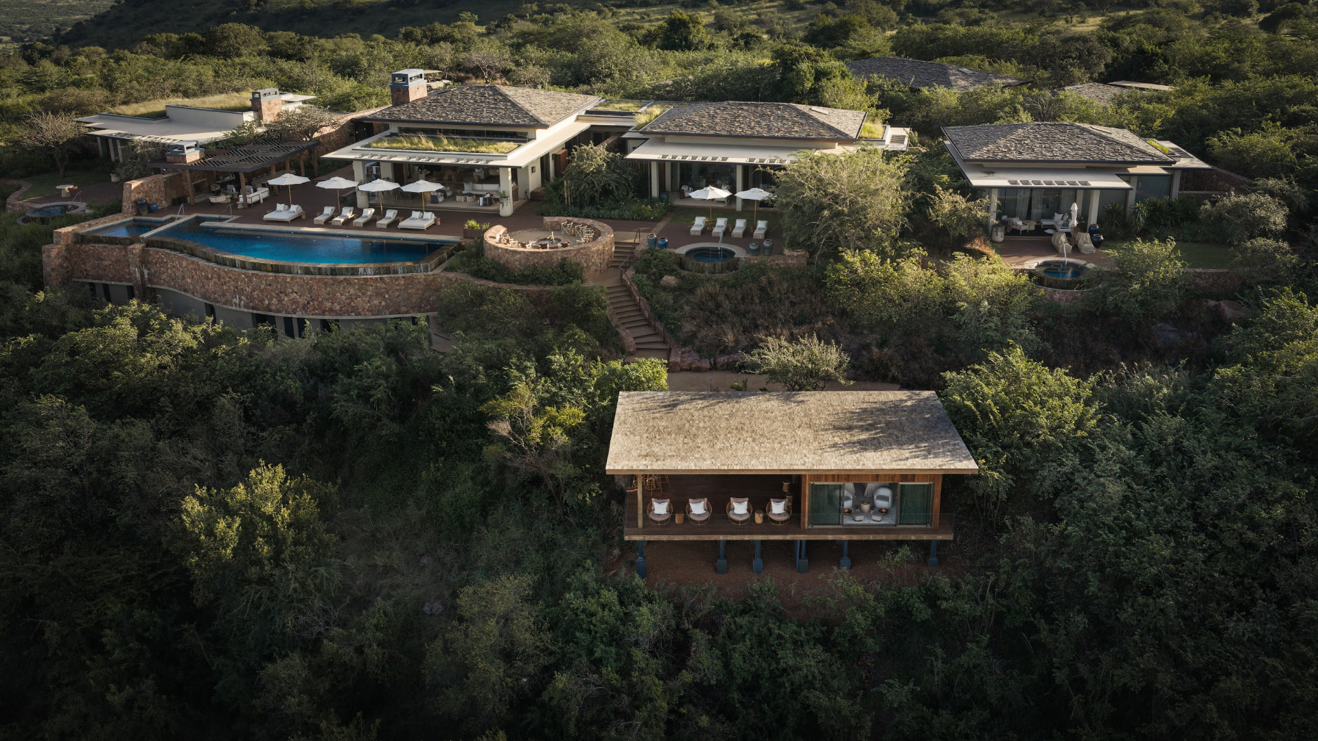 Aerial view of a private safari lodge and pool set into green hills