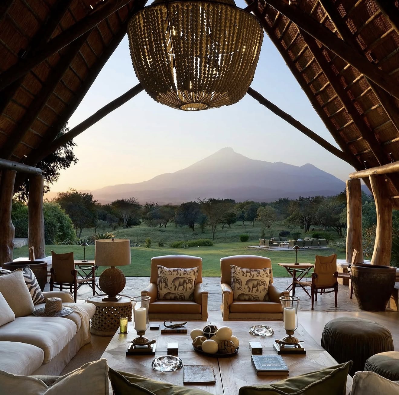 Thatched lodge lounge open to a mountain at sunrise