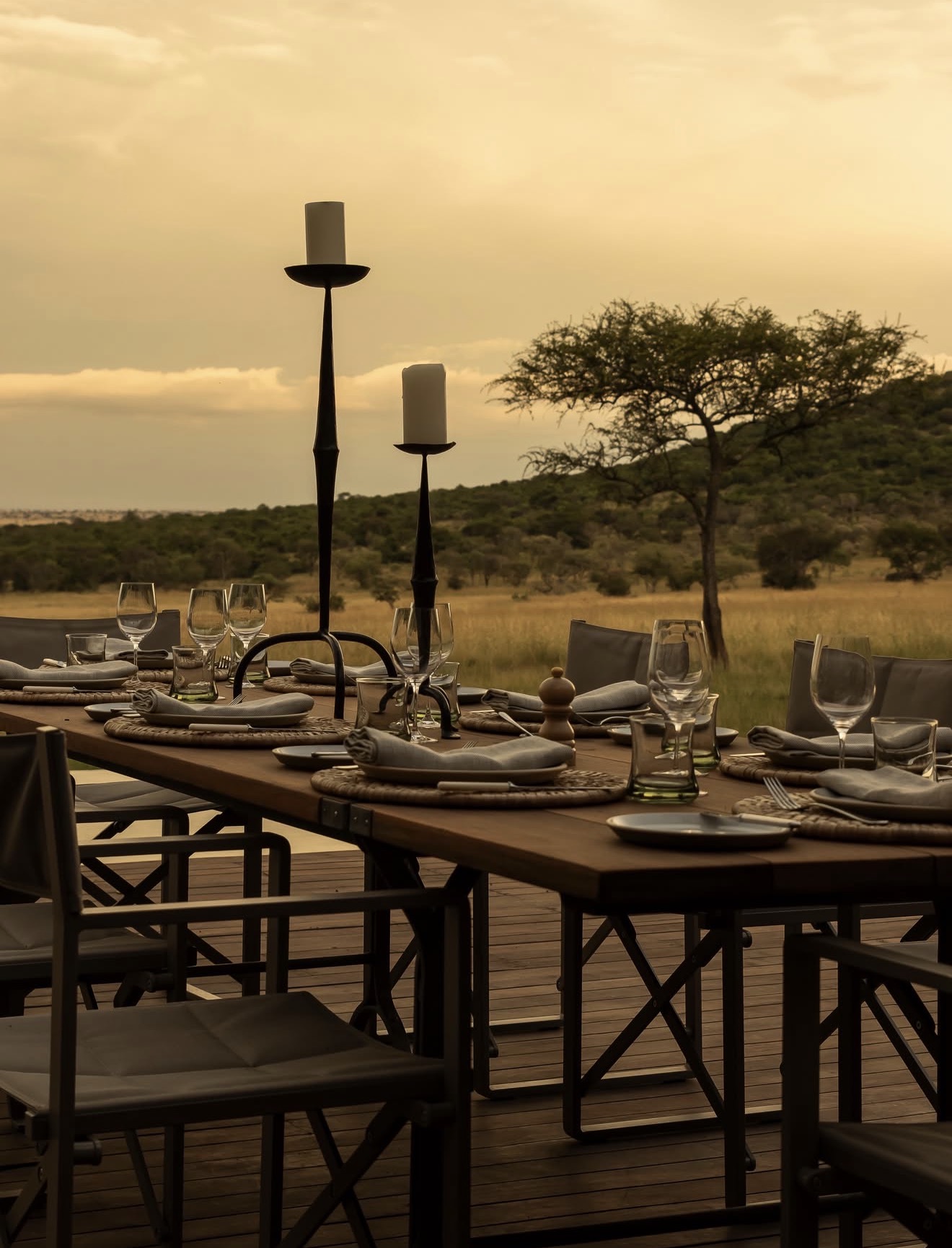 Candlelit dining table set on a deck above the plains at dusk