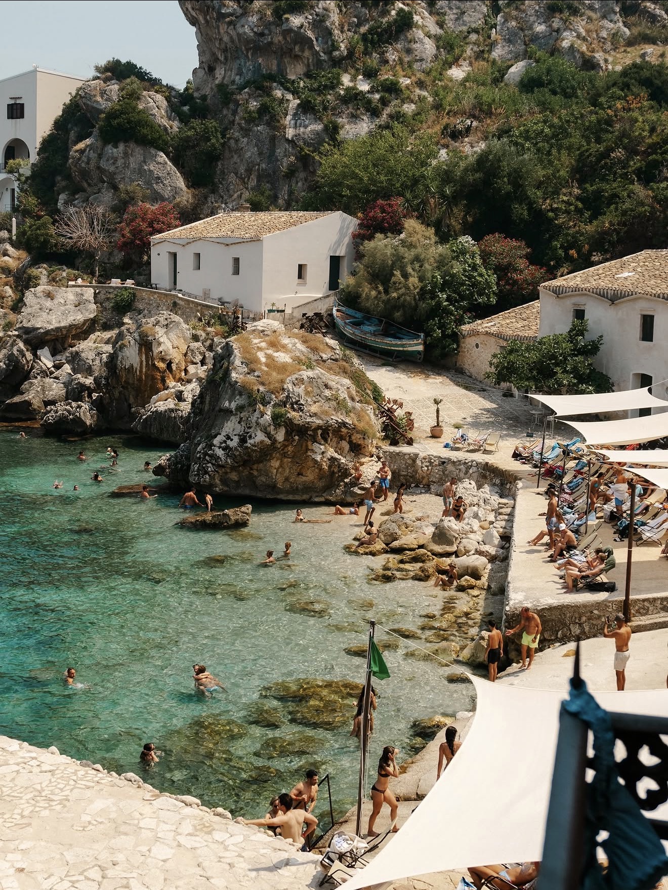 Turquoise cove at Scopello with old tuna-fishery houses, shade sails and swimmers