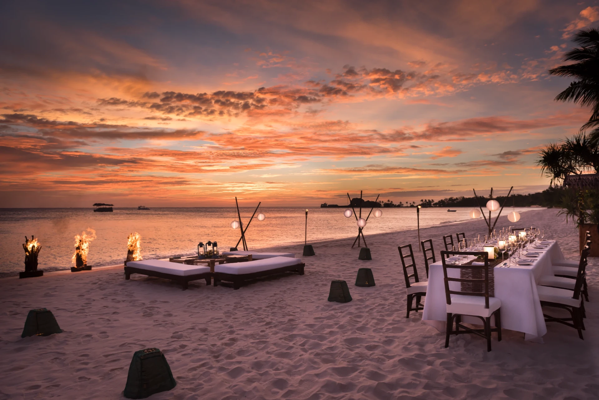 Private beach dinner prepared beneath a vivid island sunset