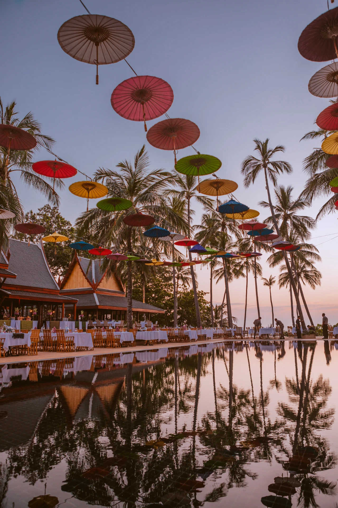 Colourful parasols suspended above a palm-lined Thai resort at dusk