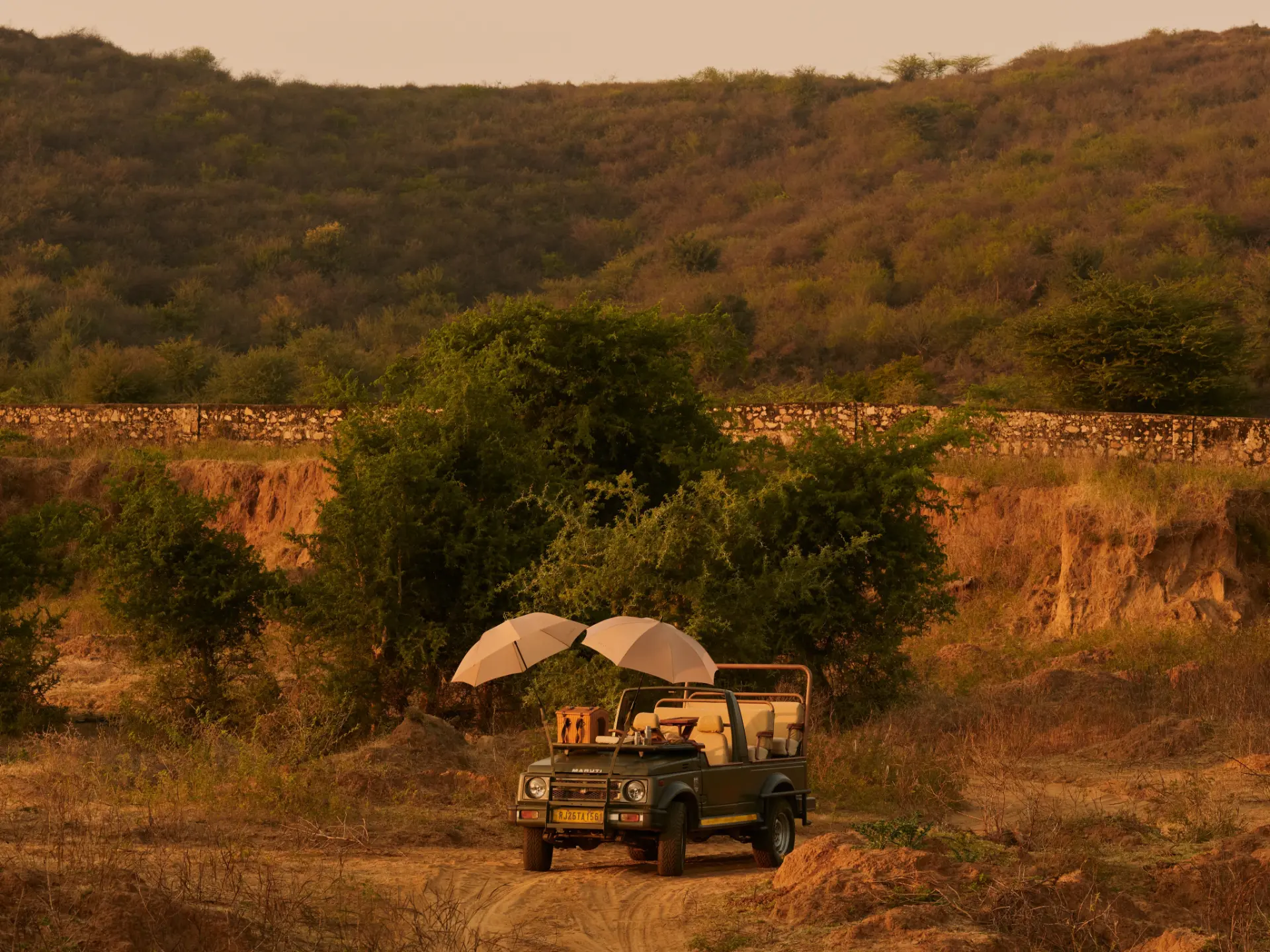 An open safari jeep with canvas umbrellas parked on a dusty track beneath wooded hills