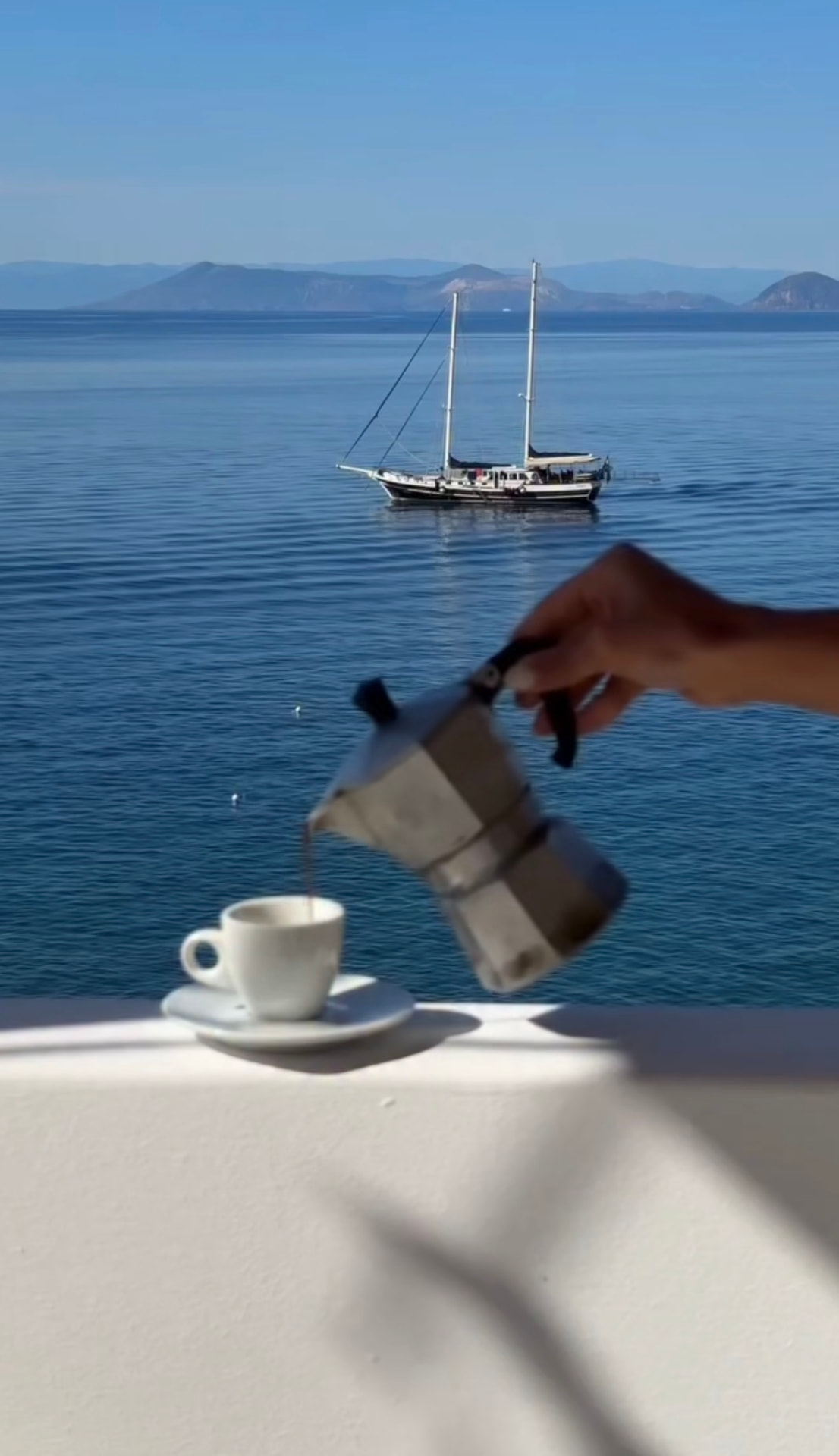 Espresso poured from a moka pot on a white terrace wall above a moored sailing boat