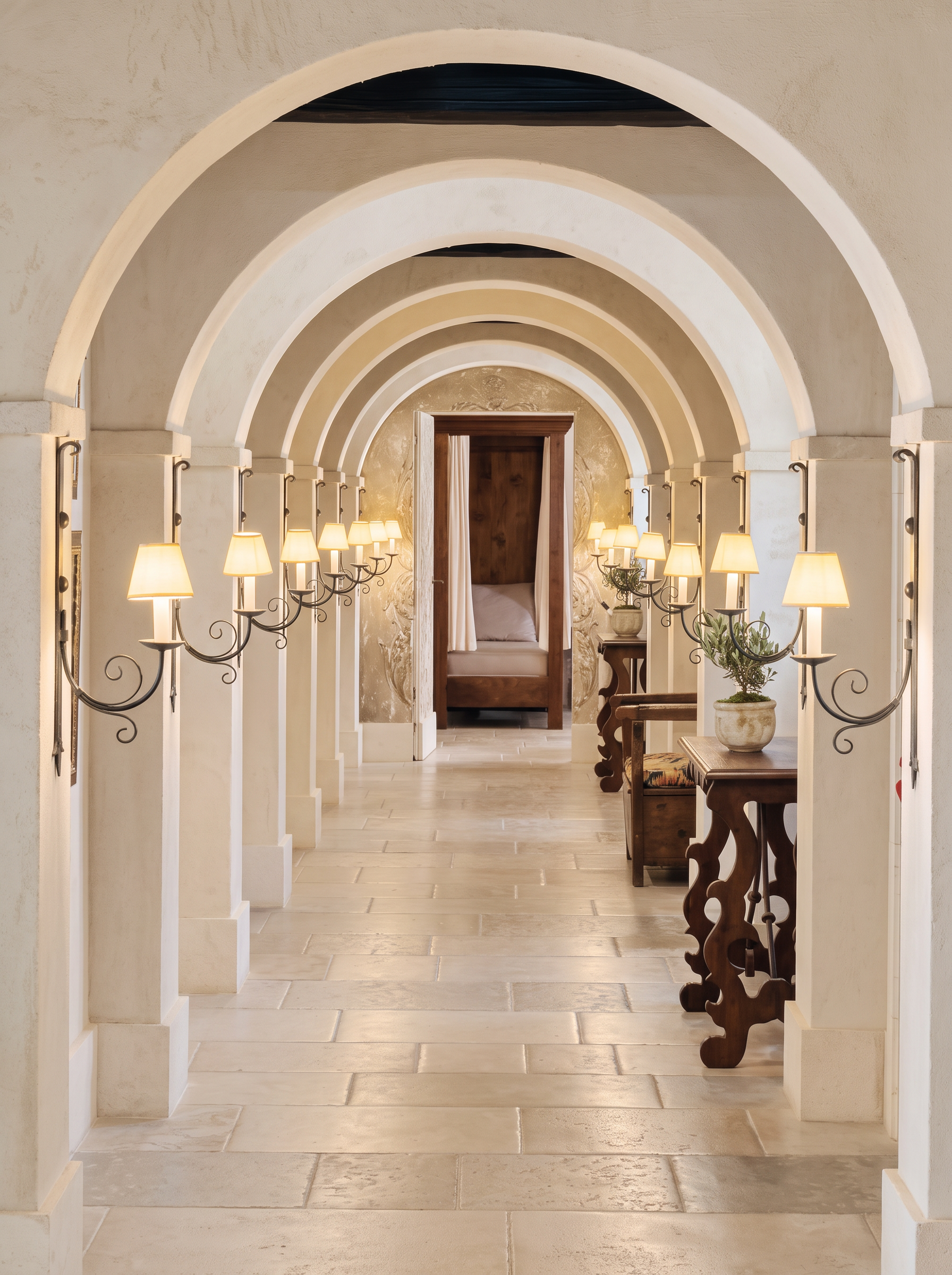 A warm cream arched hallway lined with lamps, consoles and repeating architectural arches