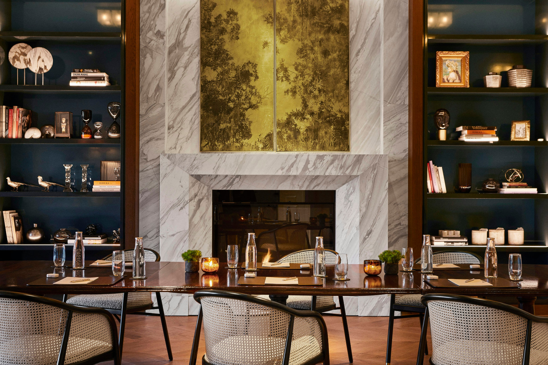 A private dining room with marble fireplace, candlelit table and curated library shelves