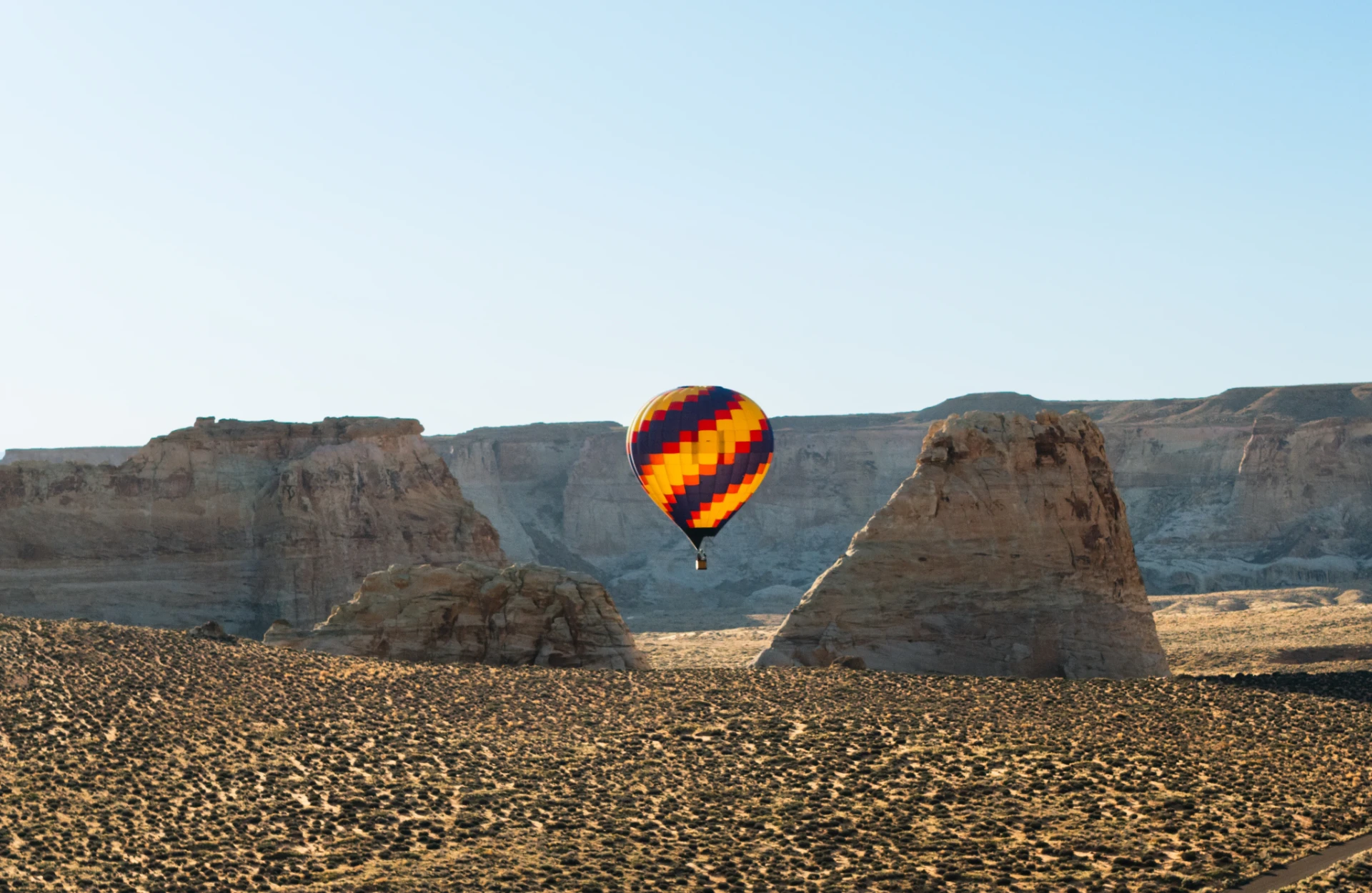A colourful hot air balloon drifting above a vast desert canyon at dawn
