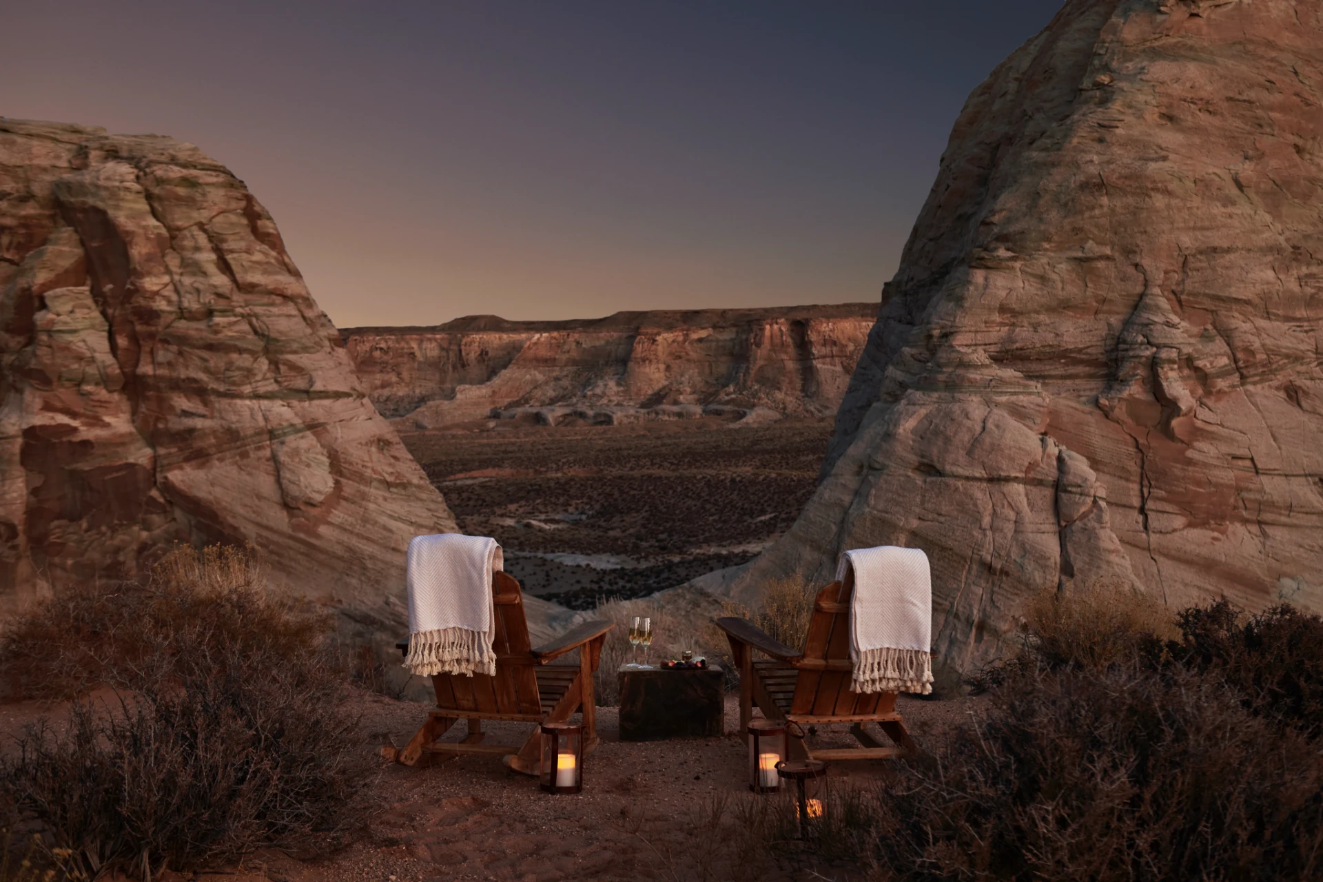 Two wooden chairs draped with white blankets overlook a vast Utah canyon at dusk